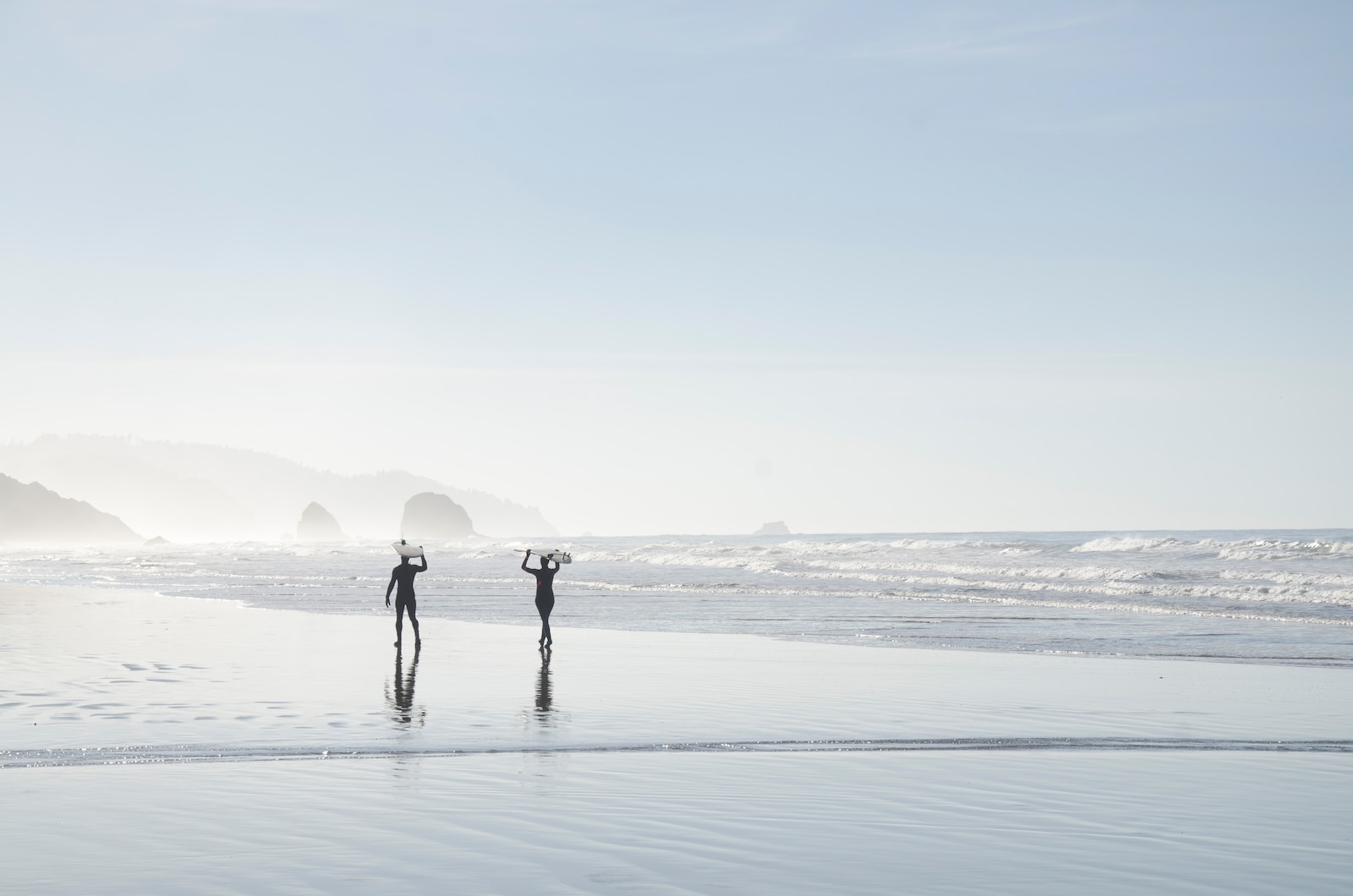 two men carrying surfboards near body of water